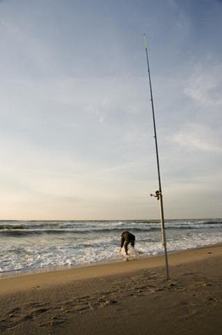 Fishing rod in a rod rest on a beach with waves breaking at the shore
