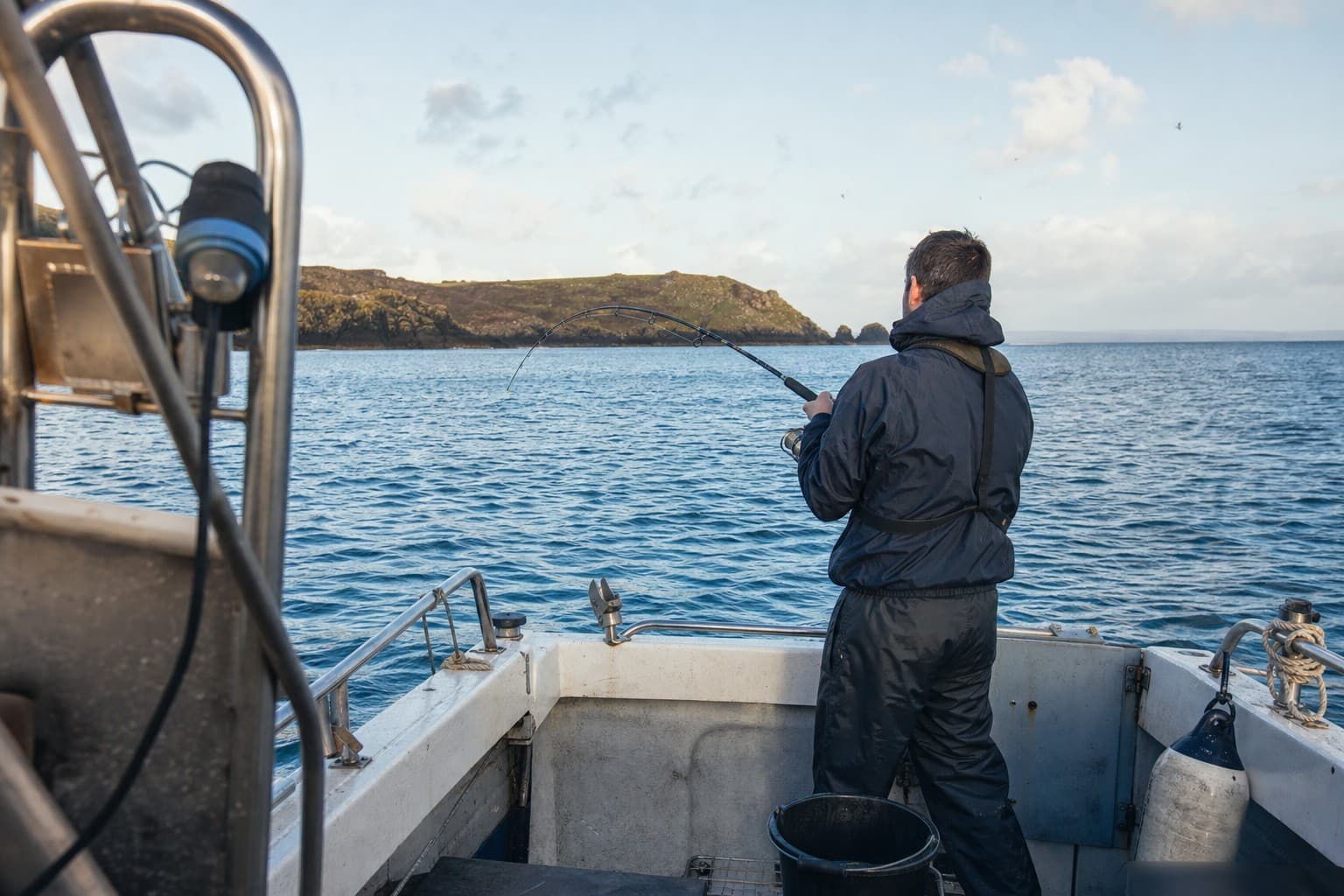 An angler fishing safely from the stern of a small boat off the Cornish coast